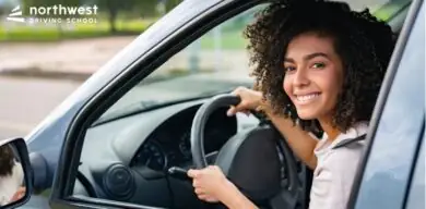 Smiling young woman in a car, showcasing Top Safety Measures while learning to drive at Northwest Driving School.