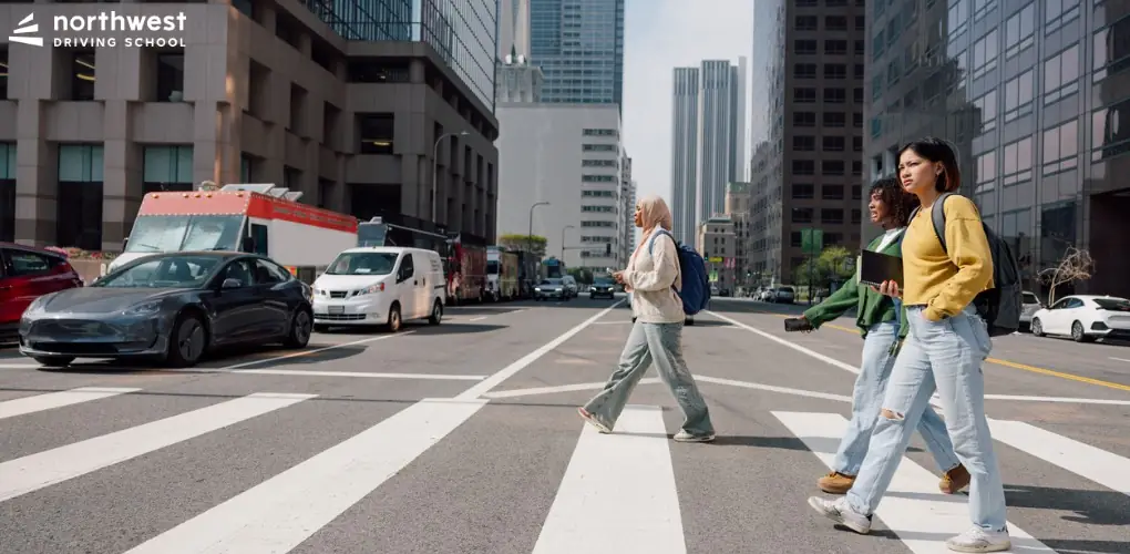 Three pedestrians cross a city street, highlighting the importance of safety in Driving Classes.