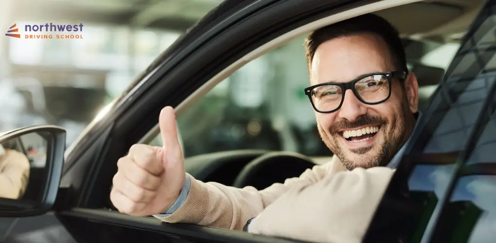 Smiling man in glasses giving a thumbs up from a car window, promoting Northwest Driving School.