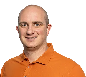 Smiling man with a shaved head wearing an orange polo shirt against a plain background.