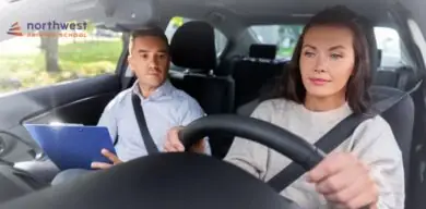 A woman drives a car while an instructor observes and takes notes.