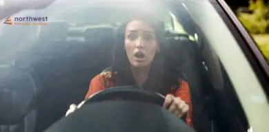 A surprised woman grips the steering wheel, looking shocked while sitting in a car.