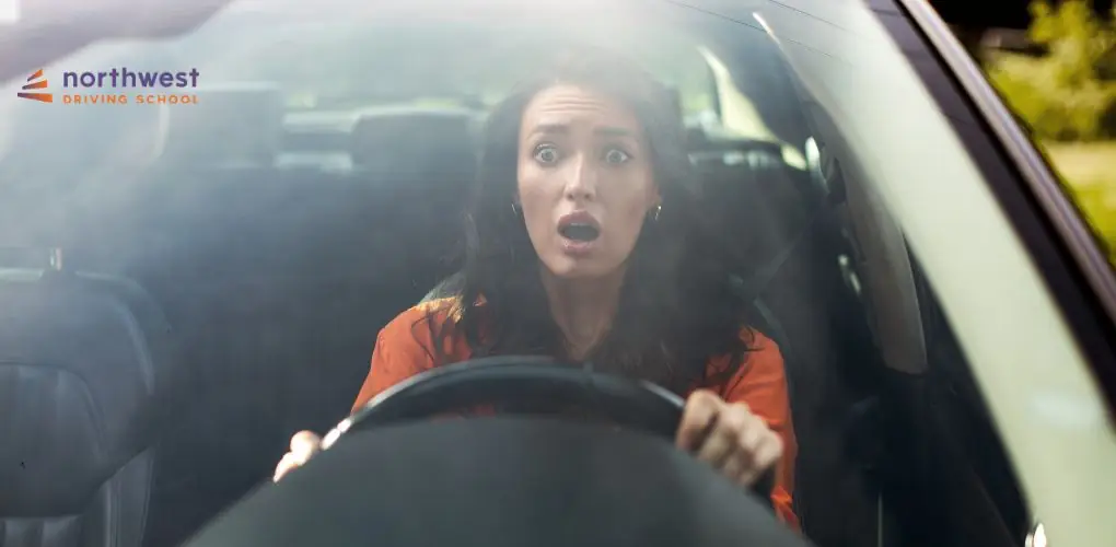 A surprised woman grips the steering wheel, looking shocked while sitting in a car.