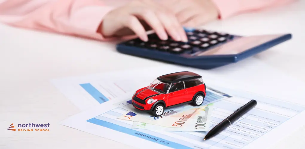 A hand using a calculator over documents, with a toy car and euro bills on the table, representing driving school finances.