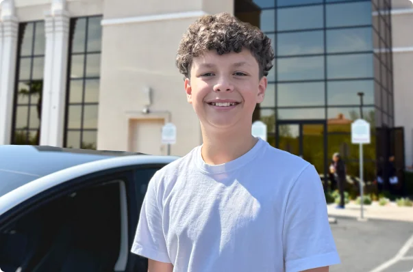 Smiling teenage student standing outside Northwest Driving School building next to a car