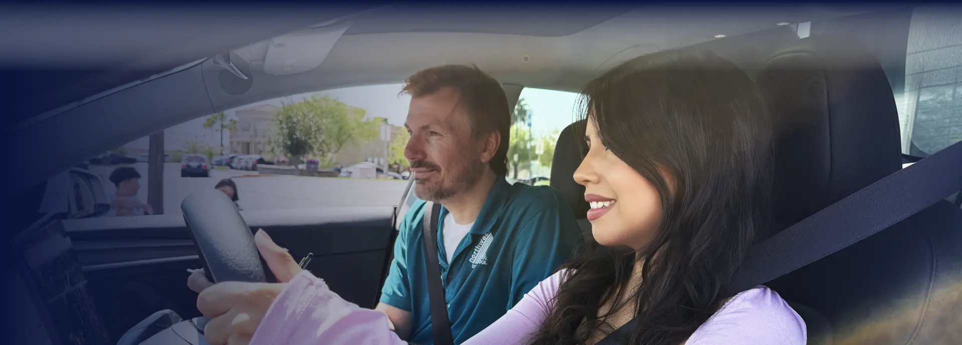 Female student driving a car with a professional instructor beside her during an in-car driving lesson
